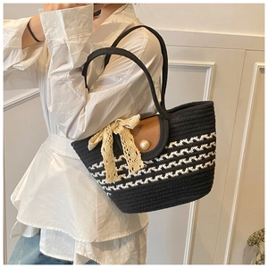 Detail of woven tote bag featuring brown leather flap, large pearl, and lace bow charm
