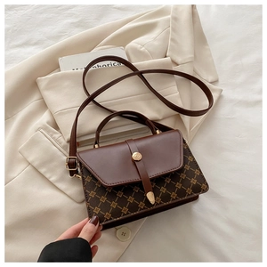 Detail of a dark brown crossbody bag with geometric patterns on a beige blazer
