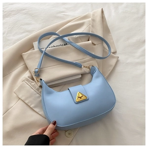 Detail of light blue crescent shoulder bag with golden triangle clasp on beige blazer