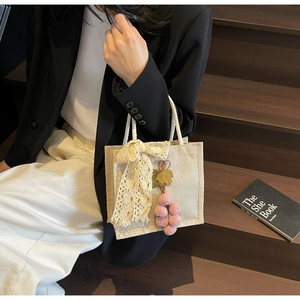 Detail of off-white canvas tote bag with lace bow and purple plush grape charm