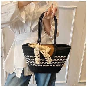 Close-up of black woven beach tote featuring white lace bow and brown leather flap