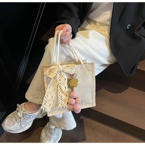 Close-up of beige linen handbag with lace bow, woven rope handles and grape charm detail
