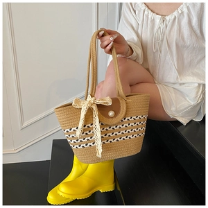 Detail of woven straw tote bag with pearl closure, lace bow and striped pattern
