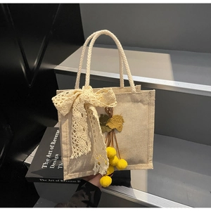 Detail of jute tote bag with white lace bow decoration and yellow fruit charm accessory