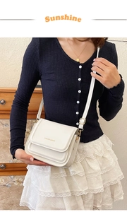 Détail du sac à bandoulière carré blanc avec inscription dorée et finitions métalliques