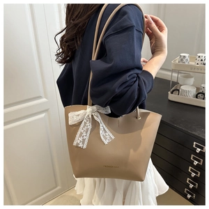Beige tote bag detail featuring white lace bow charm and Fashion Bag print on shoulder