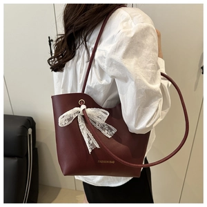 Model wearing a burgundy bucket bag with a white lace bow and gold fashion lettering