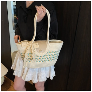 Detail of woven straw tote with blue wave patterns, pearl flap, and lace bow accent