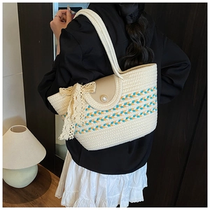 Detail of woven straw tote bag featuring striped pattern, pearl buckle, and lace bow accent