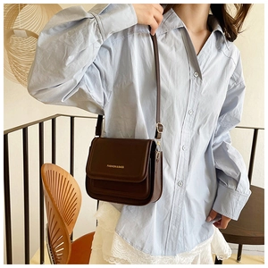Détail d'un sac bandoulière en cuir marron foncé avec boucles dorées et lettrage mode