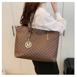 Detail of dark brown tote bag with M letter print and gold circular metal charm decoration