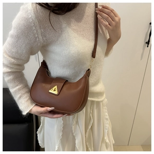 Close-up of brown leather crescent shoulder bag with golden triangle metal buckle on model
