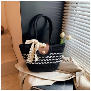 Close-up of black and white woven tote bag with leather flap and pearl button detail