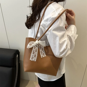 Brown minimalist tote bag with large lace bow and gold text, carried by model on shoulder