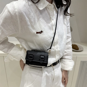 Mini black crossbody bag with carbon fiber texture worn by model in a white linen shirt