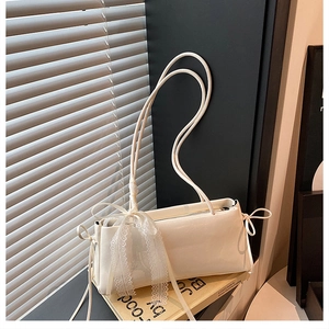 Detail of a creamy white glossy leather shoulder bag featuring lace bow and string ties