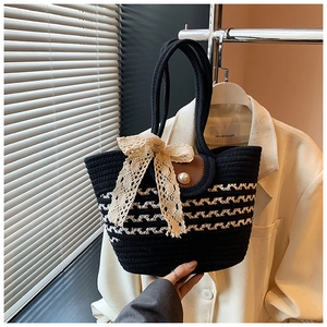 Detail of woven tote bag featuring a lace bow, pearl buckle, and dual top handles