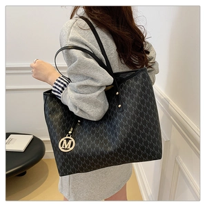 Detail of black tote bag with all-over M-letter print and round metal logo charm