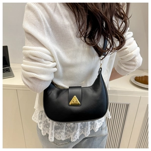 Detail of black crescent shoulder bag with golden triangle clasp on model's shoulder