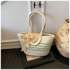 Detail of cream woven tote bag featuring lace bow and pearl clasp closure for beach