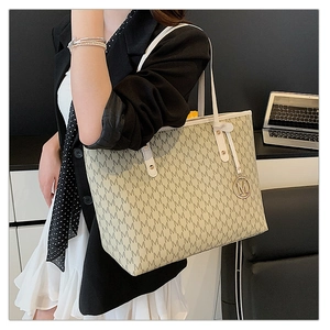 Detail of monogram tote bag featuring leather handles and iconic metallic 'M' charm