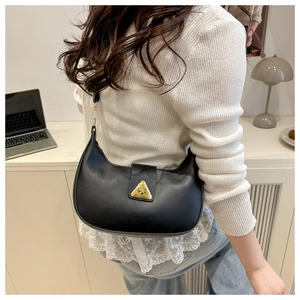 Side view of black crescent shoulder bag with golden triangle buckle on a minimal desk