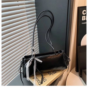 Detail of glossy black underarm bag with lace bow decoration and drawstrings