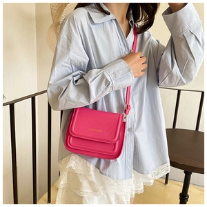 Gros plan d'un sac bandoulière rose avec lettrage doré sur une chemise bleu clair