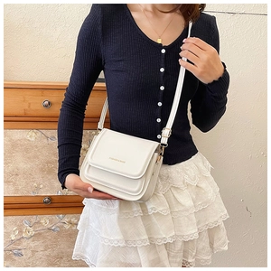 Gros plan d'un sac bandoulière blanc minimaliste avec lettrage doré sur un mannequin