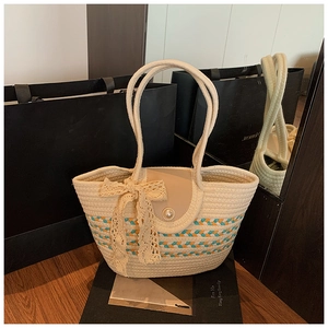 Detail of woven tote bag with pearl buckle, lace bow, and striped patterns on wood