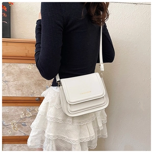 Détail du sac à bandoulière en cuir blanc avec logo doré porté par un mannequin