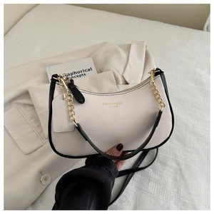 Detail of minimalist leather underarm bag with gold logo lettering and metal chain strap