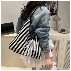 Detail of striped canvas tote bag with white lace bow and adjustable shoulder strap