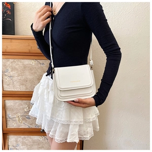 Gros plan du sac bandoulière blanc avec lettrage doré et détails de texture en cuir