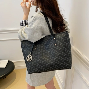 Black tote bag with M-letter monogram print and metal logo pendant shown on a model