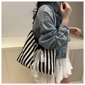 Close-up of black and white striped tote bag with lace bow detail and handmade metal tag