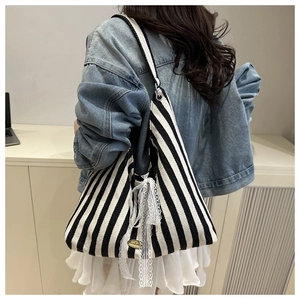 Detailed view of striped canvas tote with lace bow on model with denim jacket