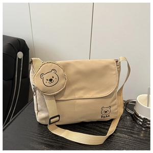Detail of beige canvas messenger bag featuring a bear print and mini bear coin purse accessory