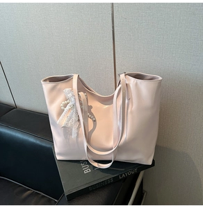 Detail of light pink tote bag with lace pearl bow charm on a leather sofa