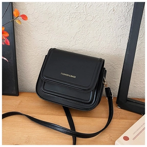 Détail du sac bandoulière noir mat avec logo doré gaufré sur une surface en bois