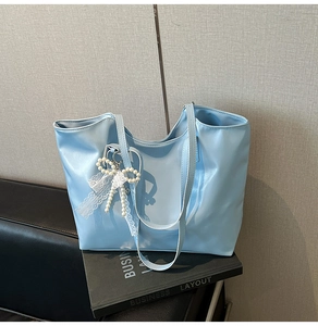 Detail of light blue faux leather tote bag with pearl lace bow charm on dark books