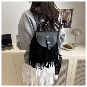 Detail of a vintage black leather backpack with long tassels and silver buckle in a modern room