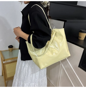 Model showing a pale yellow glossy tote bag on the shoulder in a minimalist indoor setting
