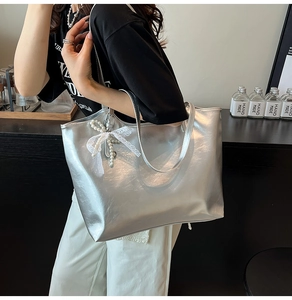 Detail view of silver metallic tote bag featuring lace bow and pearl pendant accessories