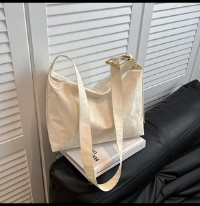 Detail of off-white pleated hobo bag with gold buckle on a black leather sofa