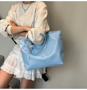 Dettaglio borsa tote in pelle verniciata azzurra con ciondolo a fiocco in pizzo e perle