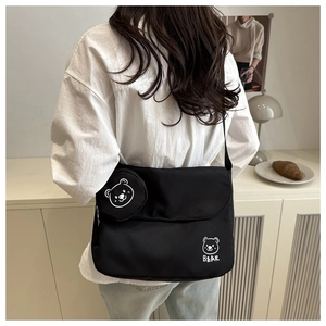 Detail of black crossbody messenger bag with a cute bear charm and logo on nylon fabric