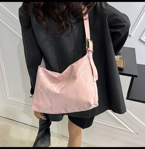 Detail of pink hobo bag with pleated texture and adjustable strap worn cross-body
