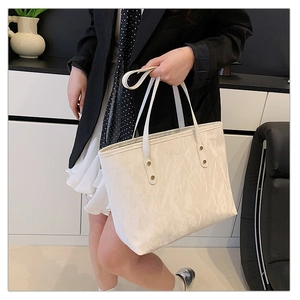 Detail view of white tote bag with pleated texture and stylish metal rivet accents