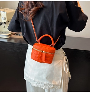 Detail of orange quilted mini chain bag worn by model in a stylish cafe setting